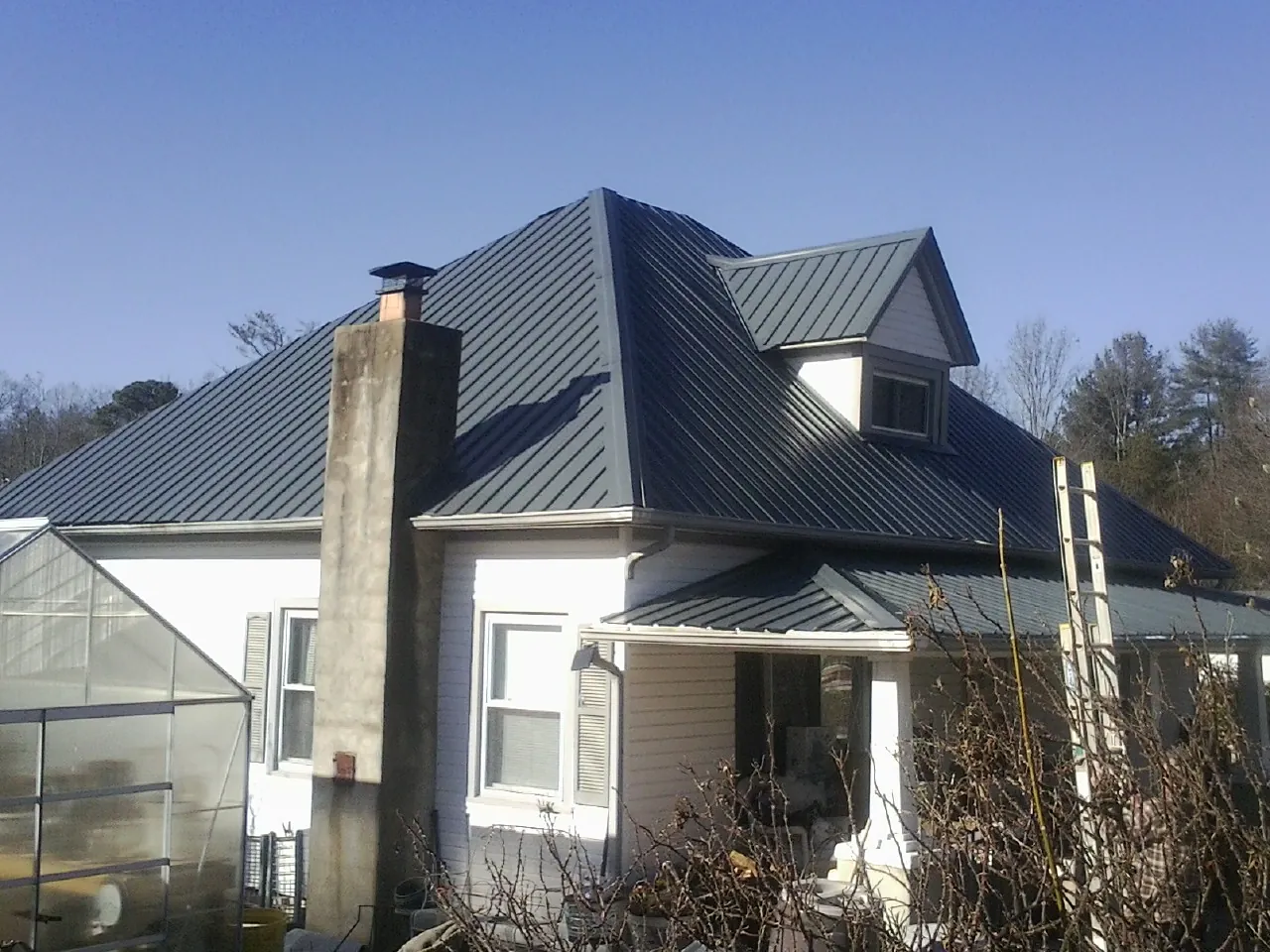 Dark blue standing seam metal roof on a white farmhouse with dormer — Slate & Tile Roof Repair by Roofing Brothers in Westbury