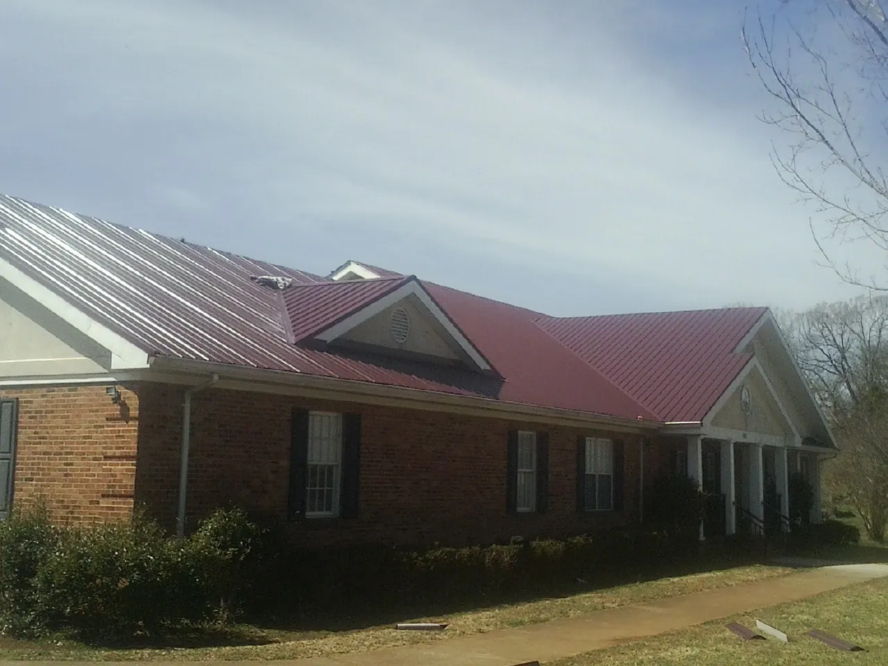 Red metal roof with gabled entries on a long brick building, from a Hail Damage Roof Repair job in Westbury