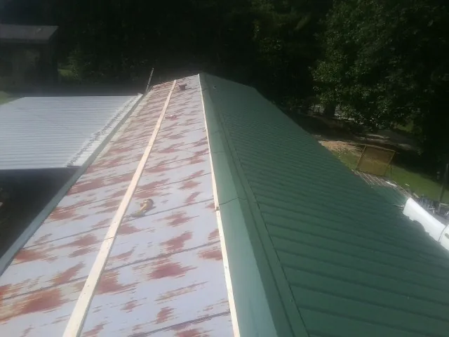 Old rusted panels beside newly installed green metal roofing — Wind Damage Roof Repair by Roofing Brothers in Westbury