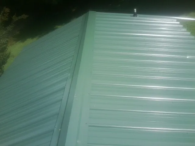 New green metal panels meeting at the ridge of a roof — Flat Roof Repair work by our crew in Westbury