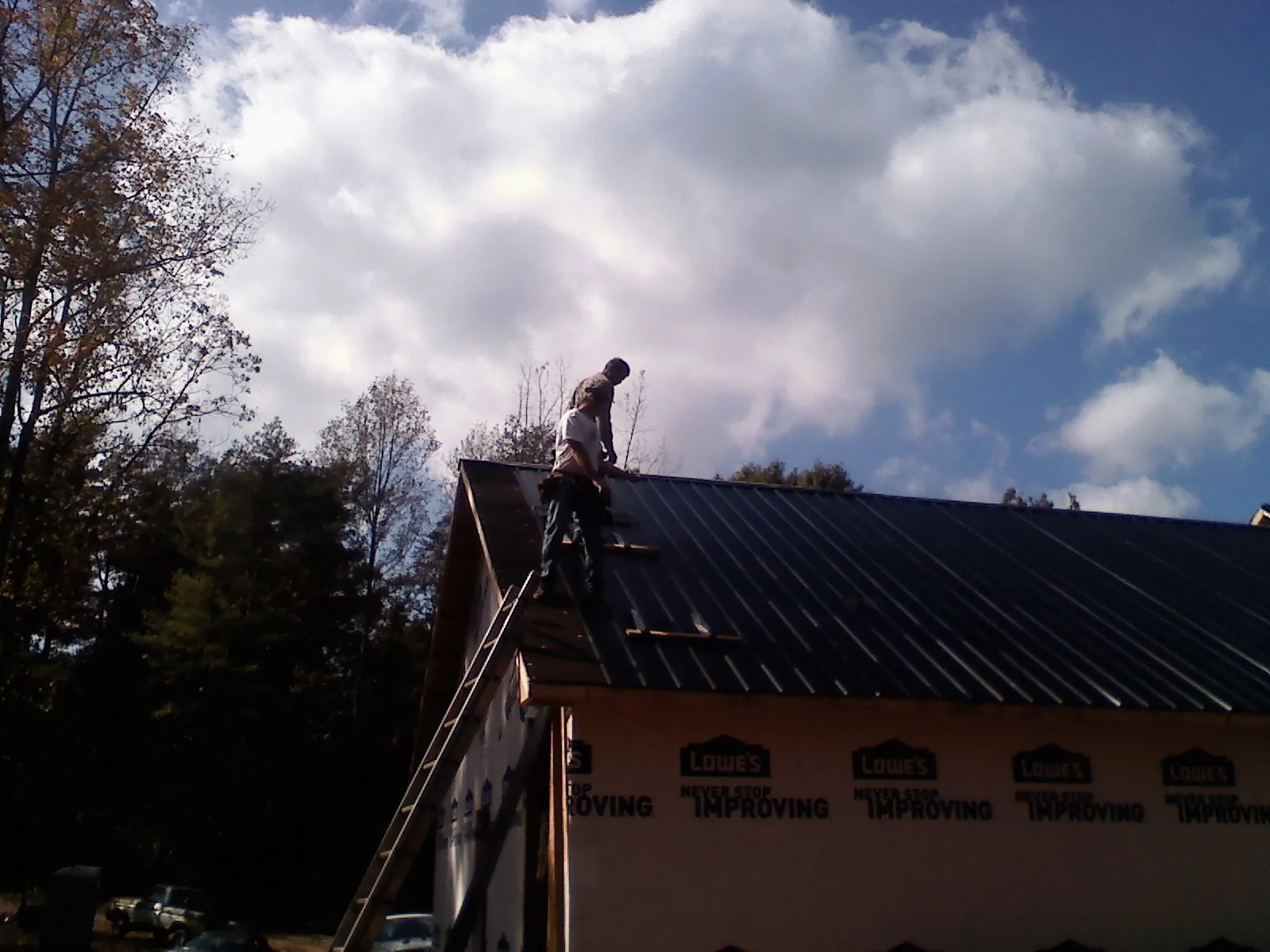 Roofer fastening dark metal panels high against a cloudy sky, from a Roof Inspection job in Westbury