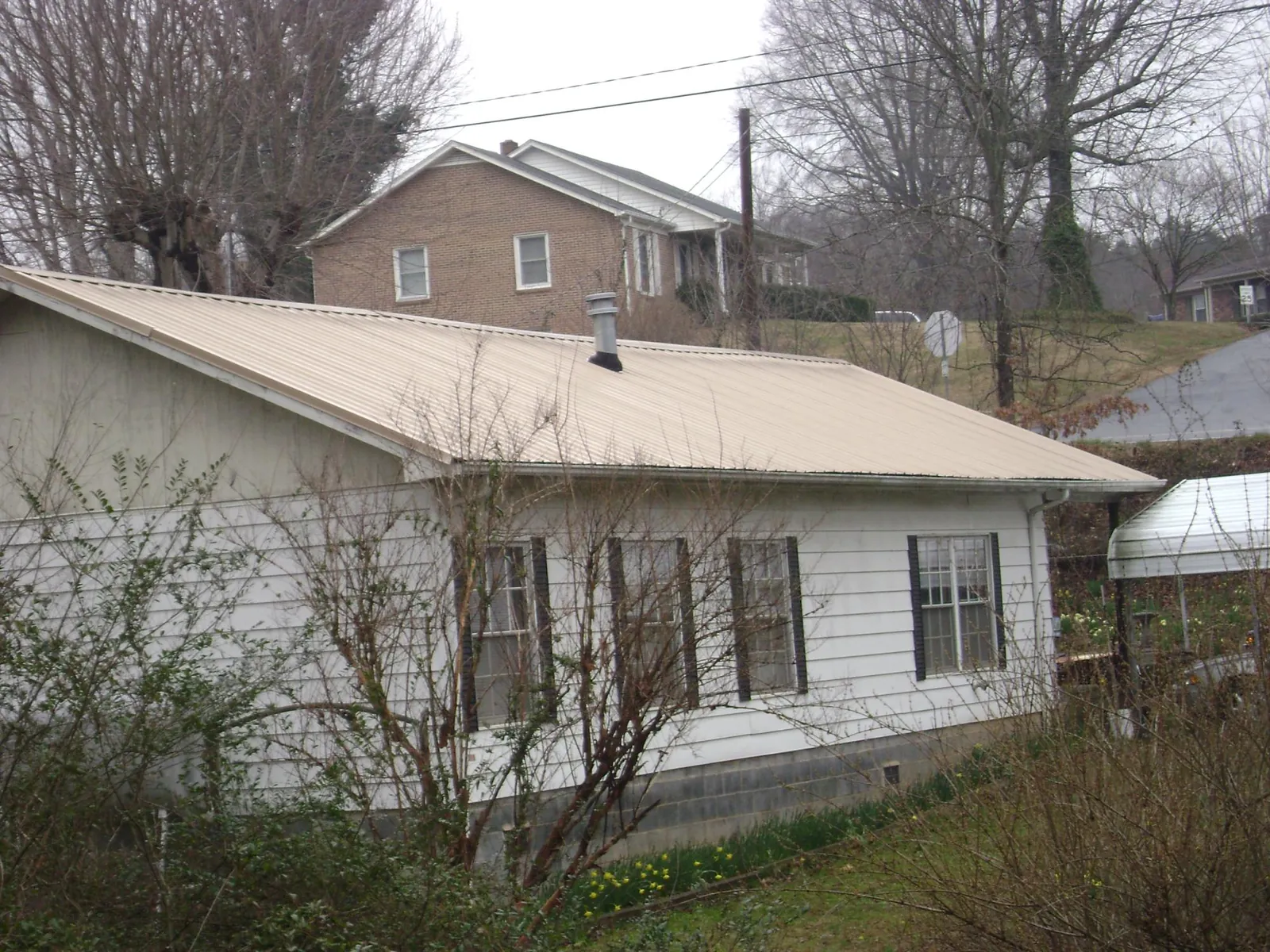 Tan metal roof on a white sided house set into a hillside — Commercial Roofing by Roofing Brothers in Westbury