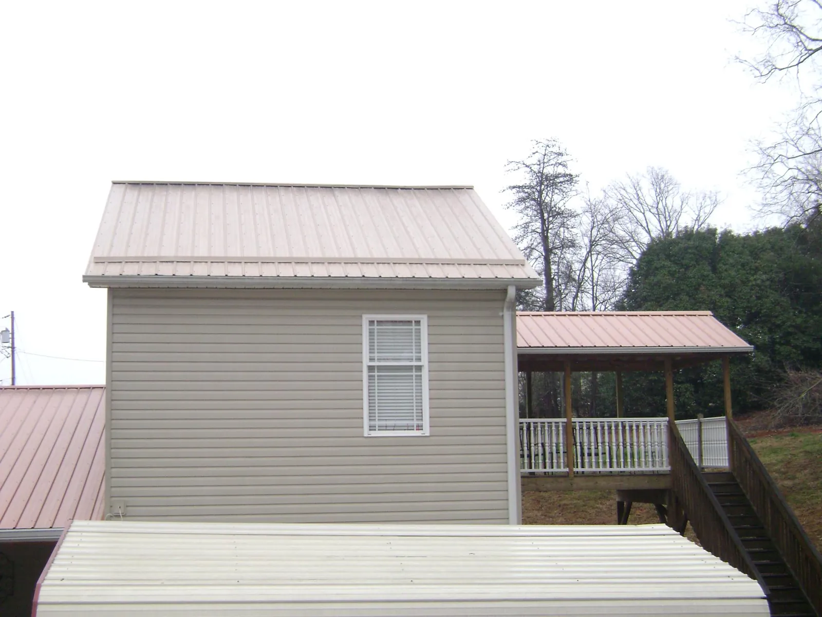 Tan metal roofs on a two story addition and attached porch, from a Roof Replacement job in Westbury